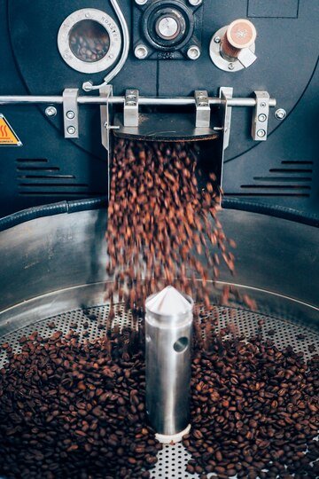 Freshly roasted coffee beans being released from a commercial coffee bean roaster into a cooling tray