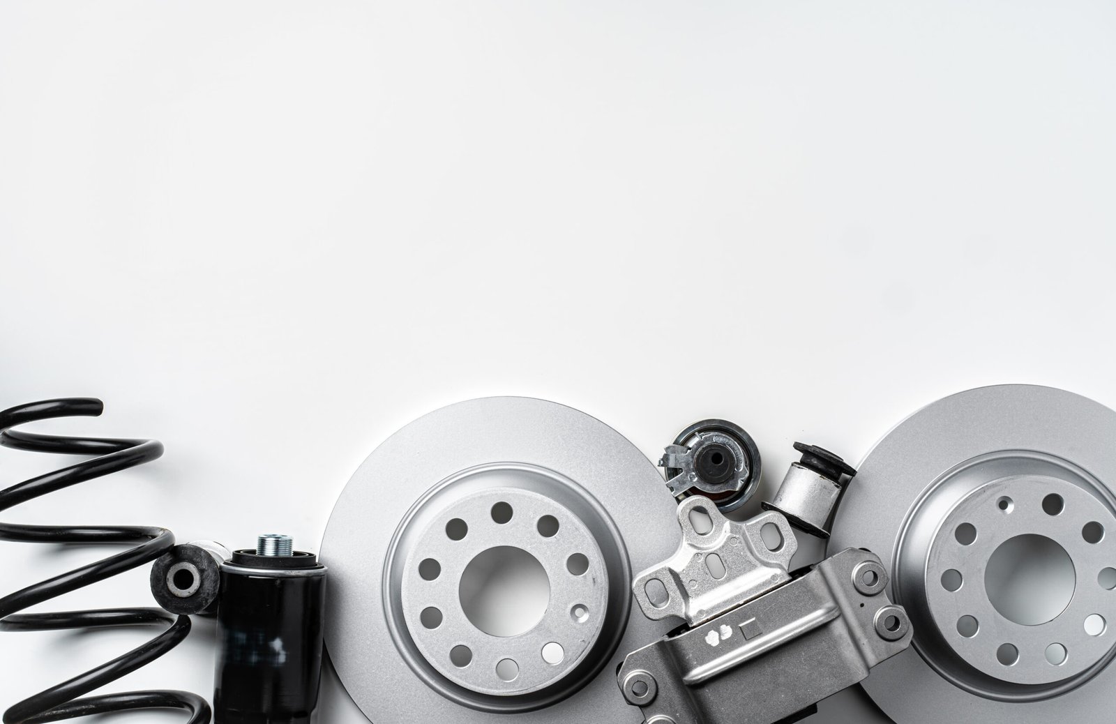 New metal car parts, including brake rotors and springs, arranged on a light grey background. Car Parts in Texas.