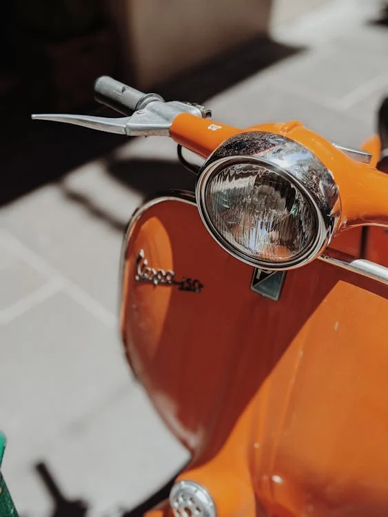 Close-up of an orange Vespa scooter with a focus on the headlight and handlebars, illustrating one of the Best Gas Scooters for Adults.