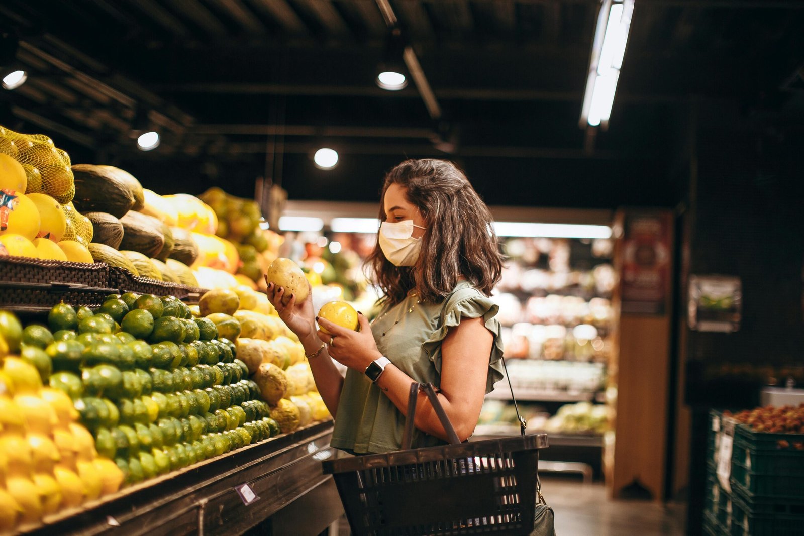 Customer wearing a mask while selecting fresh produce in a supermarket, related to the Food City Ad Next Week.