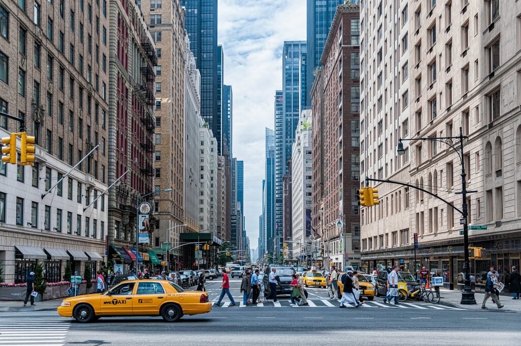 a busy city street with people crossing a street - a group of people in a room with computers - Characteristics of Laissez Faire Economics