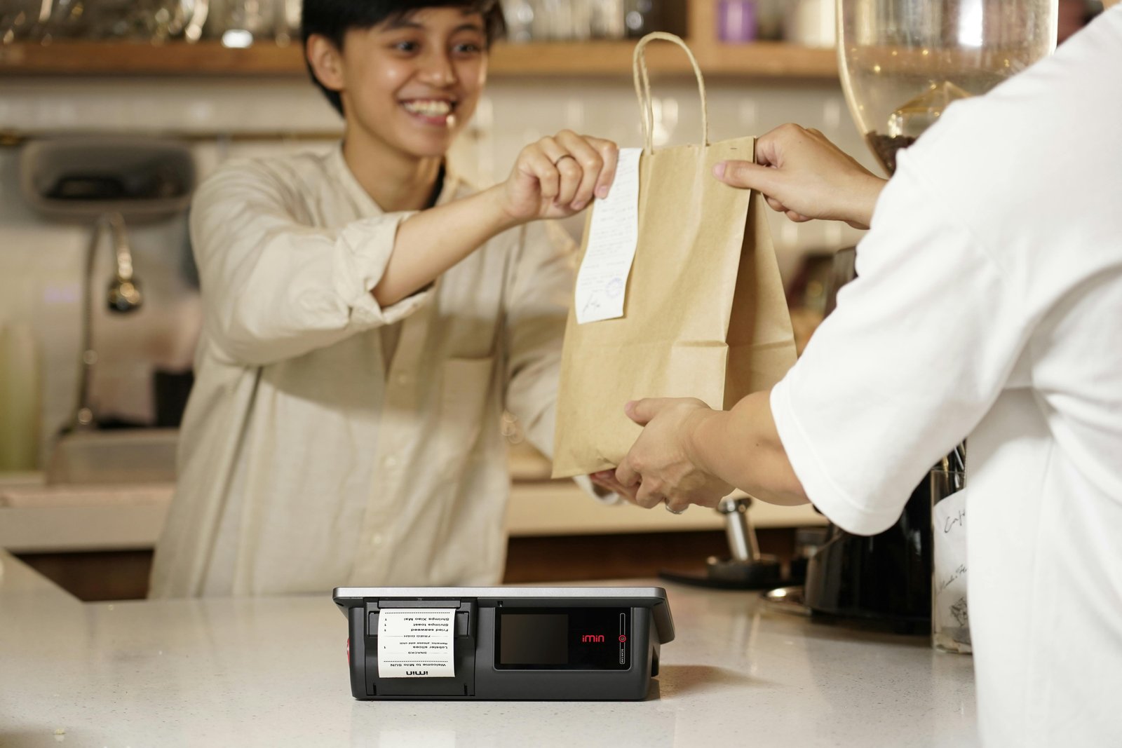 Smiling staff handing a paper bag to a customer at a counter - How to Ask for Reviews.