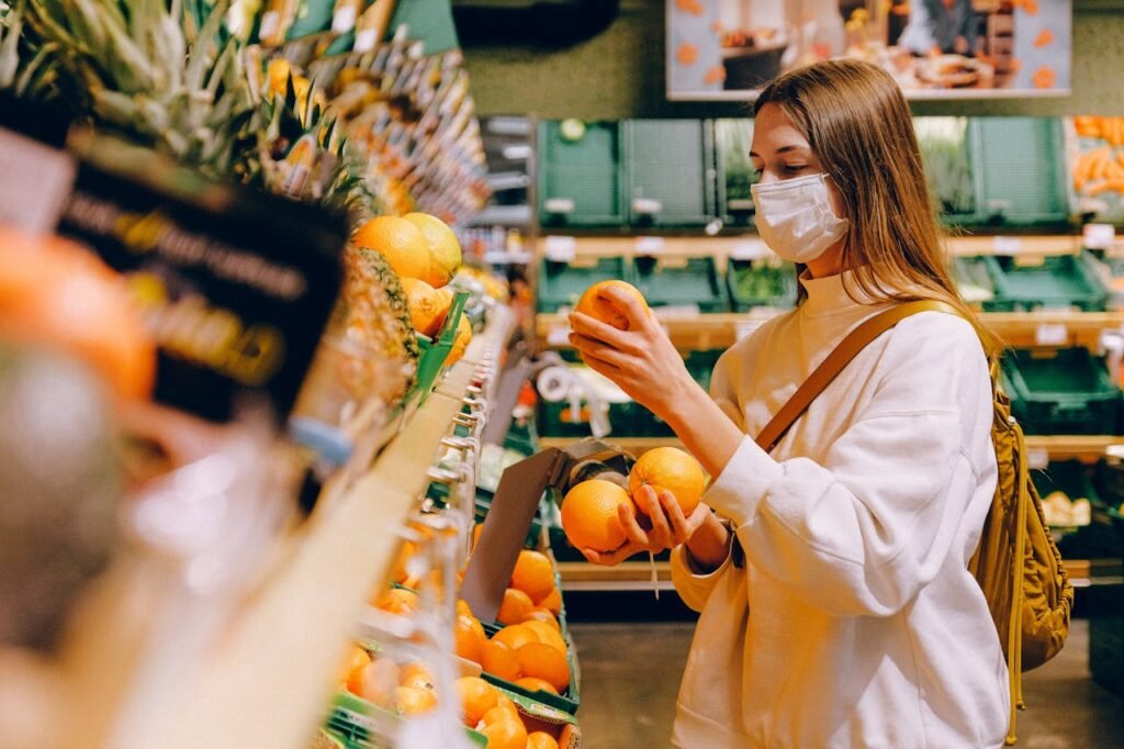 a woman wearing a face mask while holding an oranges in a grocery store - Consumer sovereignty limitations