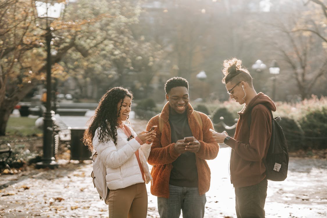 Diverse group of young people looking at their phones in a park, symbolizing community engagement within the "Woke Political Spectrum.