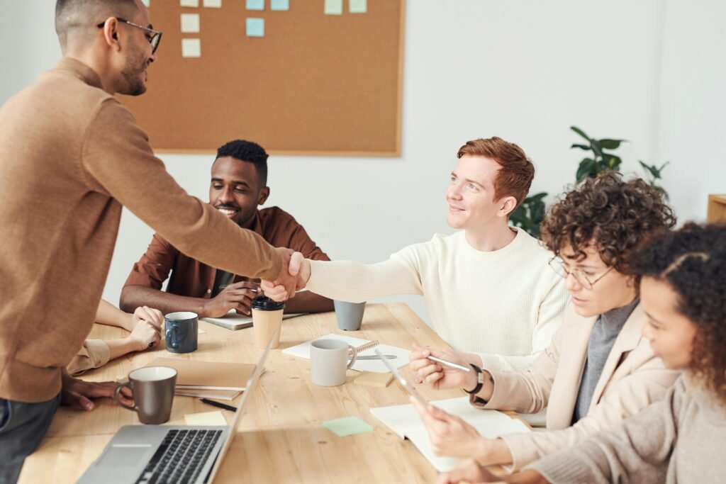 a man shaking hands with a group of people around a table - The Role of Internal Audit