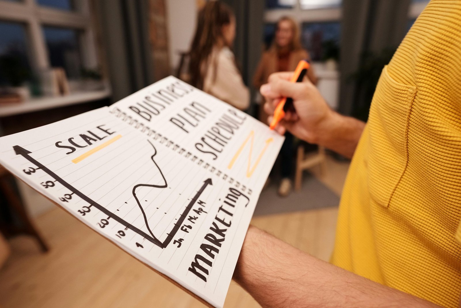 Person outlining a small business strategic planning graph in a notebook with marketing goals.