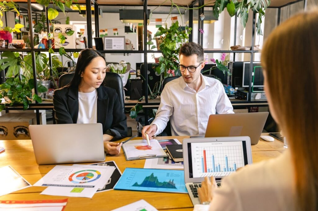 a group of people sitting around a table with laptops and papers - Growth Strategies for Business