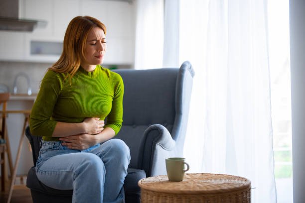 Woman having stomach ache and a tea in front of her