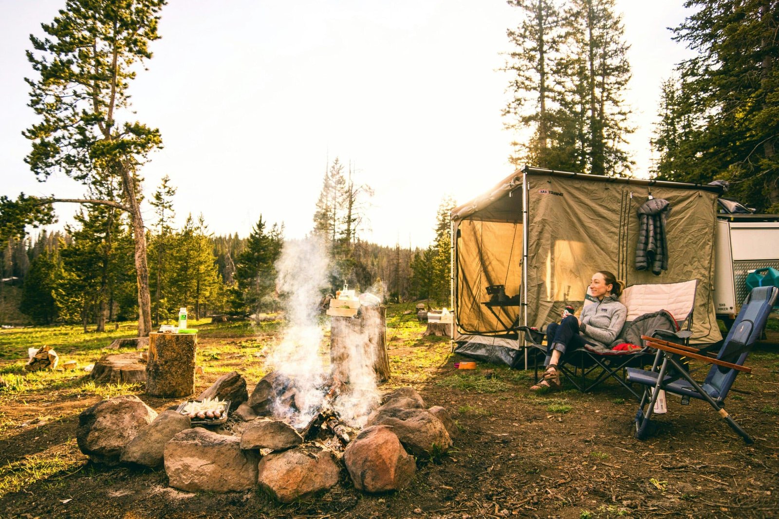 person in the woods with a big fire and camping gear