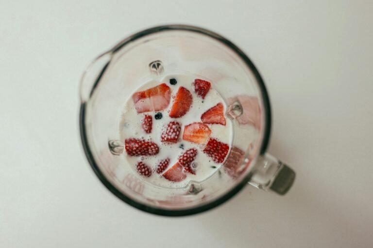 Open blender cup with strawberries, milk, and ice