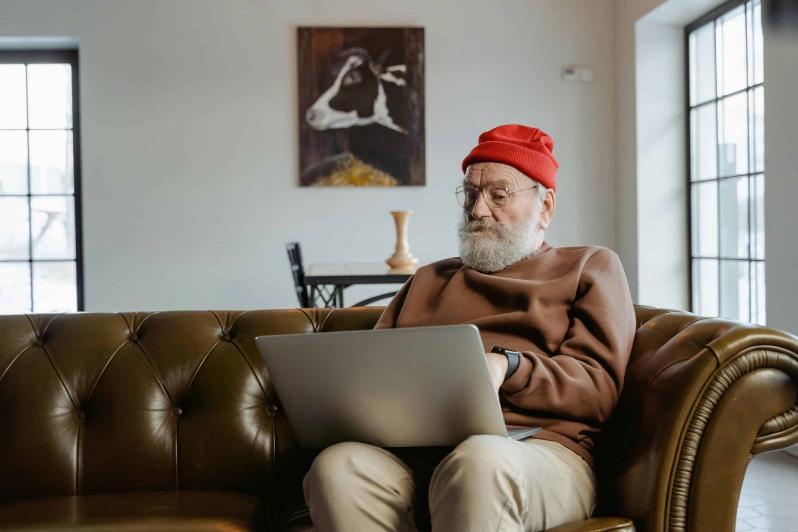 An elderly man sitting on the couch with a laptop on his lap